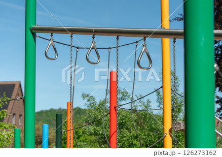 Playground structure with colorful vertical bars and metal chains under a clear blue sky. Bright and inviting, the equipment awaits children for outdoor playtime and climbing fun. Playground structure with colorful vertical bars and metal chains under a clear blue sky. Bright and inviting, the equipment awaits children for outdoor playtime and climbing fun. 126273162