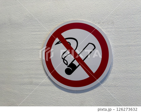 No smoking sign on light textured wall. Classic red prohibition circle with cigarette icon promotes health awareness, indoor safety, and smoke free environment compliance 126273632