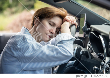 Middle aged tired woman sleeping on steering wheel exhausted from long driving in road trip. Middle aged tired woman sleeping on steering wheel exhausted from long driving in road trip. 126274329