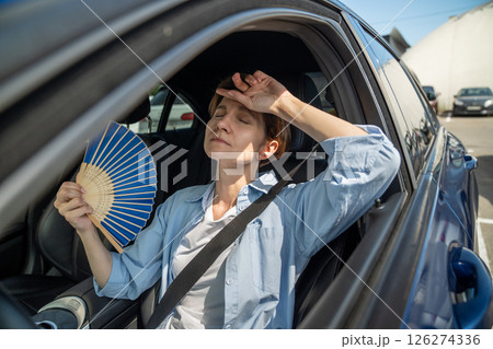 Exhausted middle aged woman drives car waves blue fan suffers from stuffiness in traffic jam. 126274336
