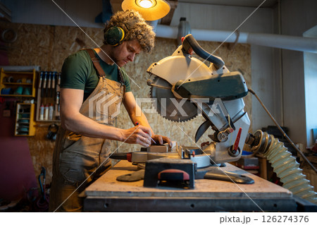 Skilled carpenter use miter saw, measure and trim wood beams in workshop. Handyman precision cut Skilled carpenter use miter saw, measure and trim wood beams in workshop. Handyman precision cut 126274376