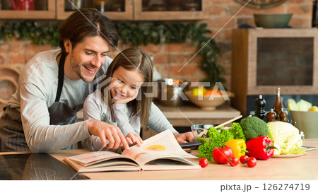 Young Father And Little Daughter Preparing Meal In Kitchen Together, Checking Recipe In Culinary Book, Cooking Healthy Lunch Or Dinner At Home, Having Fun, Enjoying Homemade Food, Free Space Young Father And Little Daughter Preparing Meal In Kitchen Together, Checking Recipe In Culinary Book, Cooking Healthy Lunch Or Dinner At Home, Having Fun, Enjoying Homemade Food, Free Space 126274719