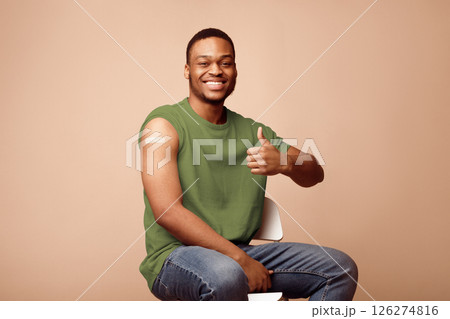 Successful Coronavirus Vaccination. Happy Vaccinated African Guy Gesturing Thumbs Up Showing Plaster On Arm After Covid-19 Vaccine Injection Posing Over Beige Background. Covid Immunization Concept Successful Coronavirus Vaccination. Happy Vaccinated African Guy Gesturing Thumbs Up Showing Plaster On Arm After Covid-19 Vaccine Injection Posing Over Beige Background. Covid Immunization Concept 126274816