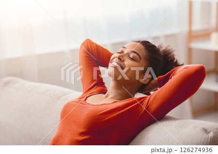 Enjoying Weekend. Happy Afro Girl Relaxing Sitting On Couch Holding Hands Behind Head At Home Enjoying Weekend. Happy Afro Girl Relaxing Sitting On Couch Holding Hands Behind Head At Home 126274936