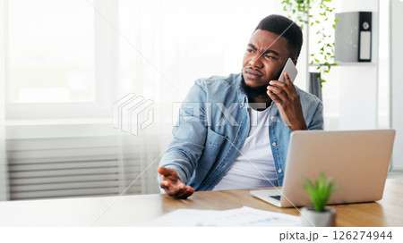 Failure and crisis concept. Upset african american employee getting bad news on phone while sitting at his workplace in office, copy space Failure and crisis concept. Upset african american employee getting bad news on phone while sitting at his workplace in office, copy space 126274944