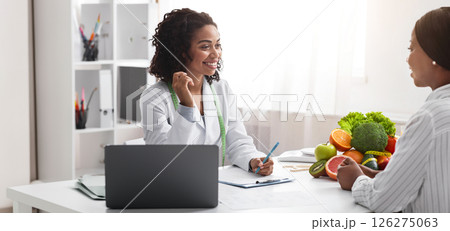 Friendly nutritionist african woman giving consultation to patient in her clinic, nutrition and diet concept, copy space Friendly nutritionist african woman giving consultation to patient in her clinic, nutrition and diet concept, copy space 126275063