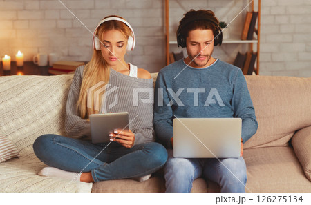Gadgets. Couple In Headphones Using Laptop And Digital Tablet Sitting On Sofa Indoor. Selective Focus 126275134