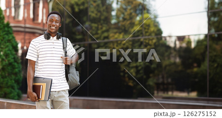 Happy smiling african american student guy with backpack and workbooks over university background, looking at camera and smiling Happy smiling african american student guy with backpack and workbooks over university background, looking at camera and smiling 126275152
