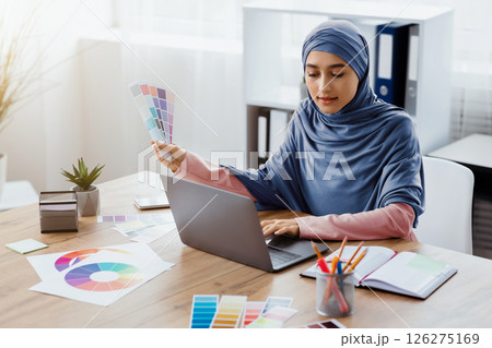 Modern Profession. Portrait of busy arabic female graphic designer working on new project with color swatches and laptop in office, free space Modern Profession. Portrait of busy arabic female graphic designer working on new project with color swatches and laptop in office, free space 126275169