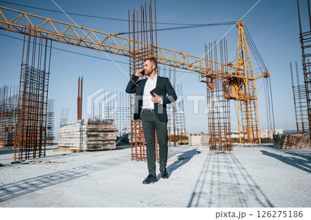 Talking by phone. Businessman in formal clothes is on the construction site at daytime 126275186