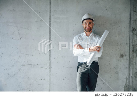 Leaning on the wall. Holding paper with project plan. Man is working on the construction site at daytime 126275239