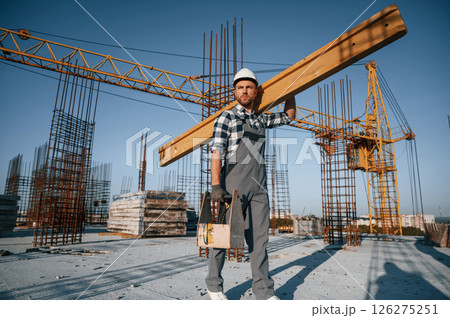Holding big wooden piece. Man is working on the construction site at daytime 126275251