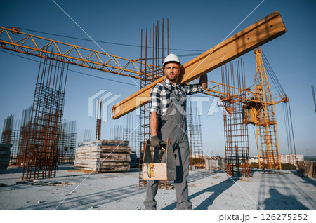 Holding big wooden piece. Man is working on the construction site at daytime Holding big wooden piece. Man is working on the construction site at daytime 126275252