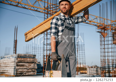Holding big wooden piece. Man is working on the construction site at daytime 126275253