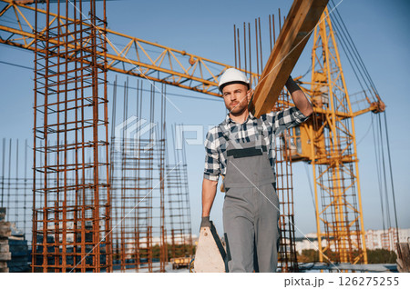 Crane behind. Holding wooden piece. Man is working on the construction site at daytime Crane behind. Holding wooden piece. Man is working on the construction site at daytime 126275255