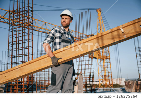 With big wooden plank in hand. Man is working on the construction site at daytime With big wooden plank in hand. Man is working on the construction site at daytime 126275264