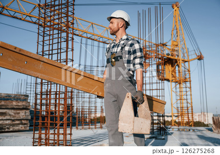With big wooden plank in hand. Man is working on the construction site at daytime 126275268