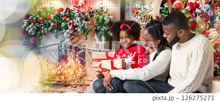Christmas gift from parents. Cute little african girl holding Xmas present, sitting with her mom and dad in decorated living room 126275271