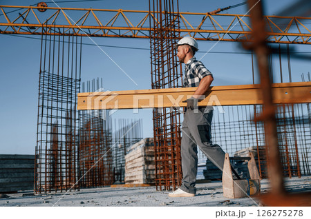 View from the side. Walking and holding wooden plank. Man is working on the construction site at daytime 126275278