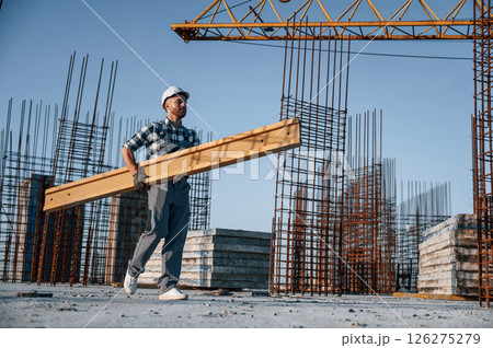 View from the side. Walking and holding wooden plank. Man is working on the construction site at daytime 126275279