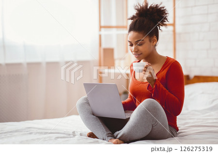 African American Lady Using Laptop Having Coffee Sitting On Bed At Home Relaxing On Weekend Morning. Empty Space, Selective Focus 126275319