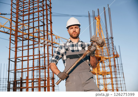 With big hammer in hands. Man is working on the construction site at daytime With big hammer in hands. Man is working on the construction site at daytime 126275399