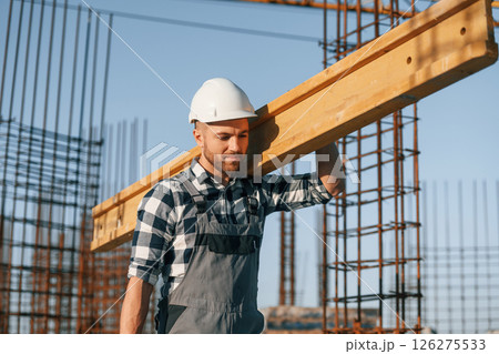 Man is working on the construction site at daytime. With wooden plank 126275533