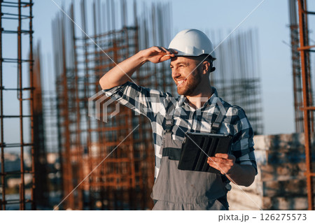 Looking to the side. Holding tablet. Man is working on the construction site at daytime 126275573