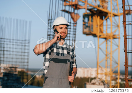 Beautiful man is working on the construction site at daytime and talking by phone 126275576
