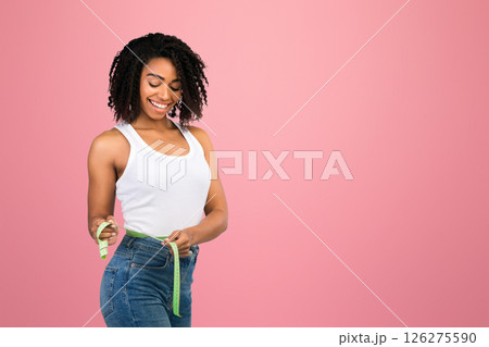Weight Loss. Smiling black girl measuring her waist using tape after diet. Free space 126275590