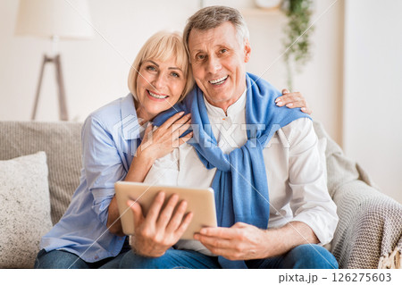 Excited mature couple with digital tablet smiling to camera, woman embracing husband Excited mature couple with digital tablet smiling to camera, woman embracing husband 126275603