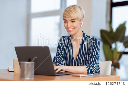 Mature Secretary Lady Working On Laptop In Earphones Sitting In Modern Office. Successful Business Career. Selective Focus Mature Secretary Lady Working On Laptop In Earphones Sitting In Modern Office. Successful Business Career. Selective Focus 126275748