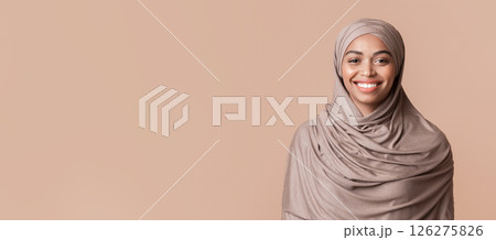 Portrait of modest black muslim girl in hijab smiling at camera, posing over yellow background, empty space 126275826