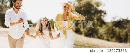 Happy parents walking with daughter, holding hands and spending time together in countryside Happy parents walking with daughter, holding hands and spending time together in countryside 126275888