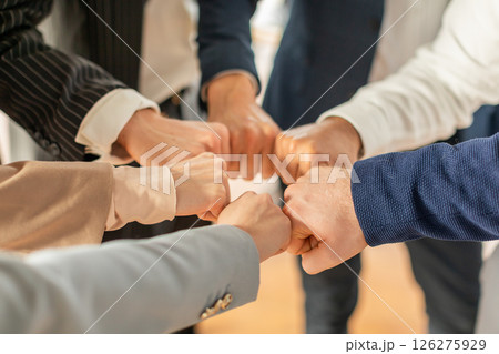 Several people, likely colleagues, stand in a circle and bump fists together. They are wearing business attire, suggesting they are in a professional setting, cropped Several people, likely colleagues, stand in a circle and bump fists together. They are wearing business attire, suggesting they are in a professional setting, cropped 126275929