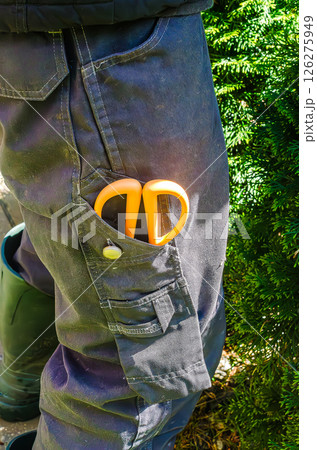 Bright orange scissors in work pants pocket in garden, sunny outdoor setting. High quality photo 126275949