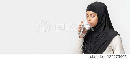Black islamic girl in hijab drinking water from glass, standing over light background in studio, closeup portrait, free space Black islamic girl in hijab drinking water from glass, standing over light background in studio, closeup portrait, free space 126275965