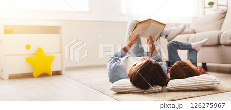 Little daughter and daddy enjoying time together, laying on floor at home, man reading book to his cute daughter, empty space 126275967