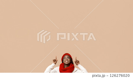 Great deal. Excited black winter woman pointing up at empty space above her head, beige studio background 126276020