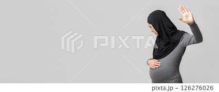 Islam And Domestic Violence Concept. Scared pregnant muslim woman in hijab doing stop gesture, hiding face and touching her belly on grey background Islam And Domestic Violence Concept. Scared pregnant muslim woman in hijab doing stop gesture, hiding face and touching her belly on grey background 126276026