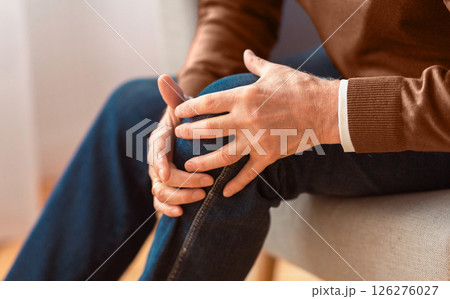Unrecognizable senior man massaging his knee suffering from arthritis pain sitting on sofa indoor. Cropped, selective focus 126276027