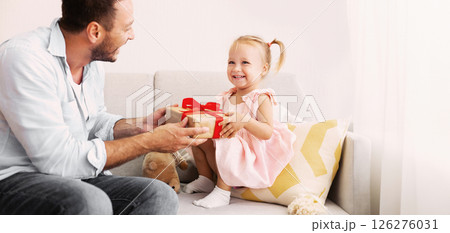 Birthday Present. Happy loving family sitting on the couch and holding gift box with red bow Birthday Present. Happy loving family sitting on the couch and holding gift box with red bow 126276031