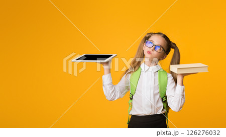 Books Or Gadgets. Nurdy School Girl Comparing Schoolbook And Digital Tablet Over Yellow Background. Empty Space Books Or Gadgets. Nurdy School Girl Comparing Schoolbook And Digital Tablet Over Yellow Background. Empty Space 126276032