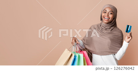 Cashback Concept. Cheerful Afro Islamic Woman In Headscarf Holding Credit Card And Shopping Bags, Yellow Background With Empty Space Cashback Concept. Cheerful Afro Islamic Woman In Headscarf Holding Credit Card And Shopping Bags, Yellow Background With Empty Space 126276042