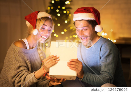 Magical surprise. Couple opening xmas gift box in living room, in front of Christmas tree 126276095