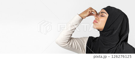 Tired afro muslim woman in hijab touching her nose bridge, suffering from eye pain, standing over light background, closeup Tired afro muslim woman in hijab touching her nose bridge, suffering from eye pain, standing over light background, closeup 126276125