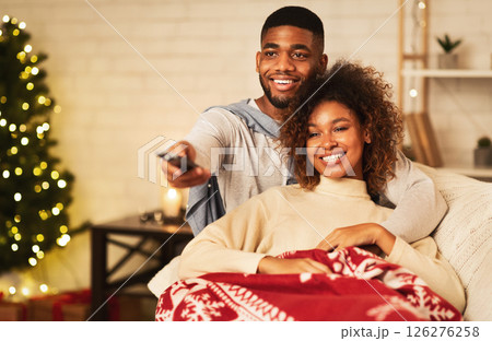 Afro couple in love at Christmas eve enjoy watching tv, lying under plaid on sofa 126276258