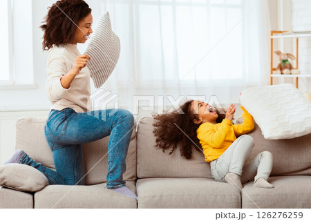 Jofyl Black Mother And Daughter Fighting With Pillows Laughing Having Fun Playing Together At Home. Selective Focus Jofyl Black Mother And Daughter Fighting With Pillows Laughing Having Fun Playing Together At Home. Selective Focus 126276259