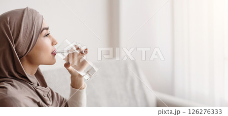 Thirsty islamic woman in headscarf drinking mineral water from glass at home, selective focus, empty space Thirsty islamic woman in headscarf drinking mineral water from glass at home, selective focus, empty space 126276333