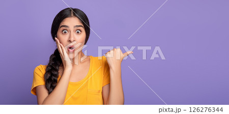 Omg, Cool Offer. Surprised young indian lady pointing at free space isolated over purple studio background. Excited shocked woman showing copy space and place for advert or promotional text, banner 126276344